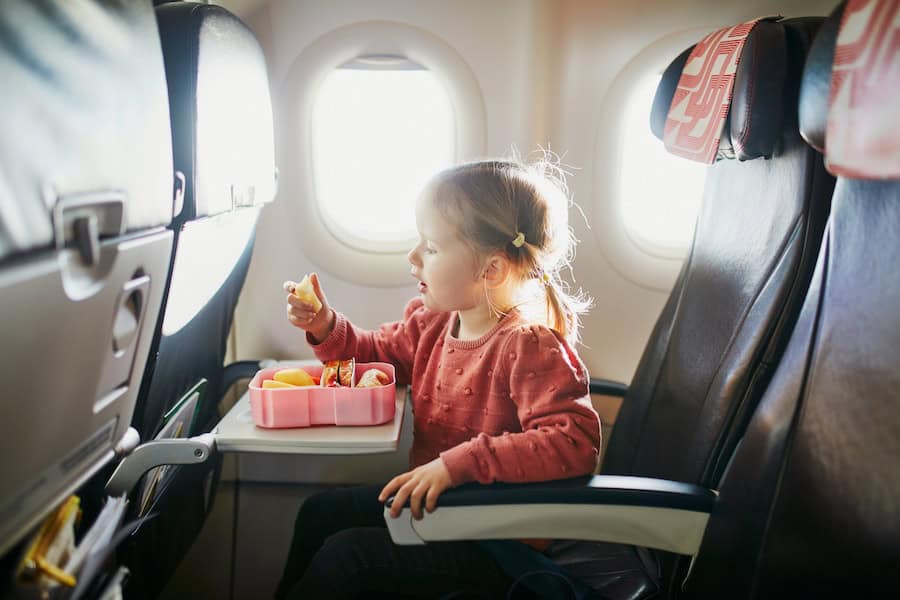 Preschooler girl eating snacks from lunch box while traveling by plane