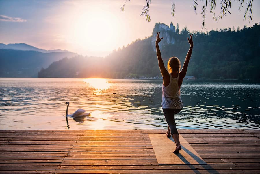 woman practicing Yoga, doing a sun salutation, by the lake, with a Swan passing by